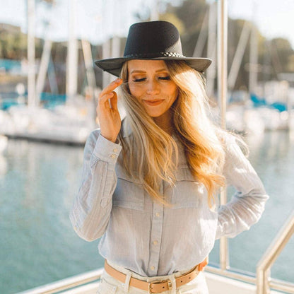 A woman standing on a boat fixing her hair wearing brown belt and a black hat