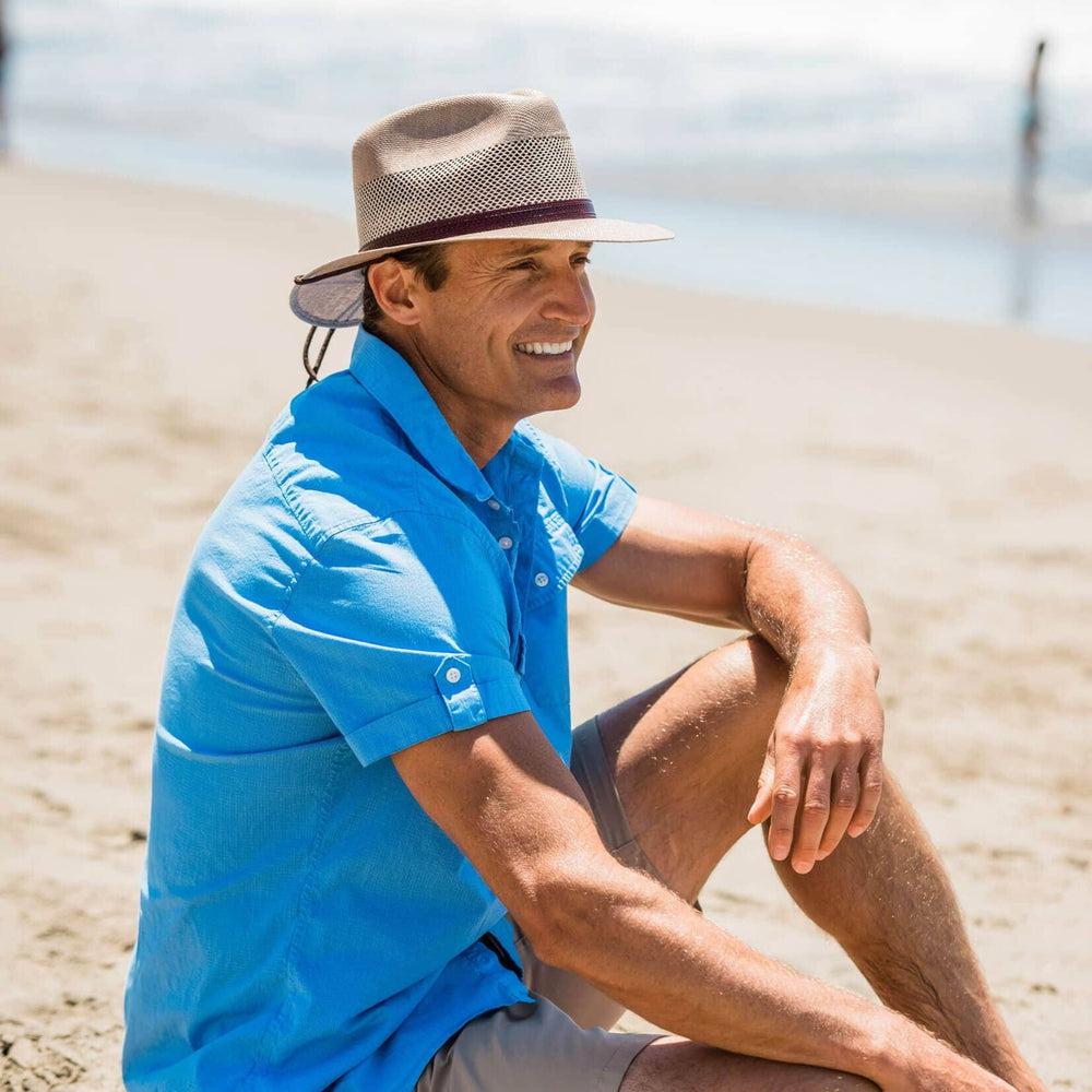 Man sitting on beach wearing the tan Milan mens sun hat by American Hat Makers