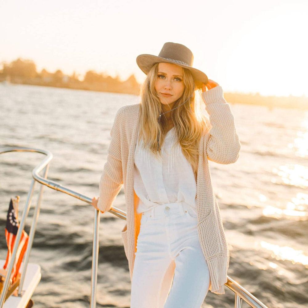 A woman on a boat lean on the metal steel and holding her hat