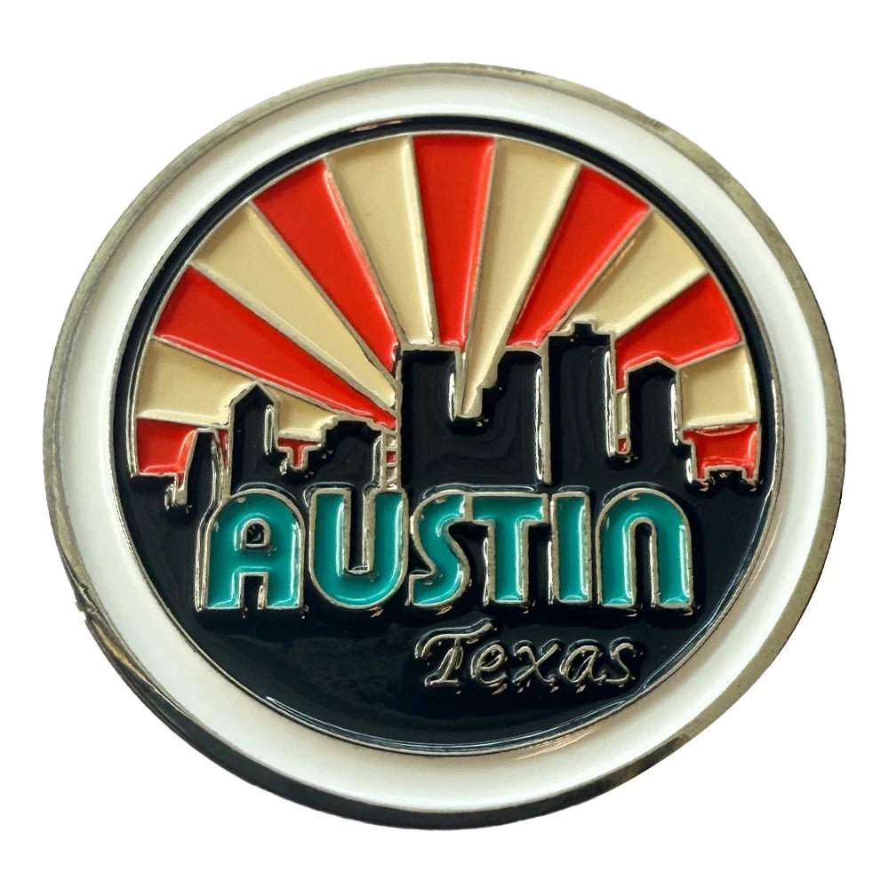 A circular Austin, Texas city emblem pin or badge featuring a black skyline silhouette against a red and cream sunburst, with the word "AUSTIN" in teal and "Texas" below on a white background.