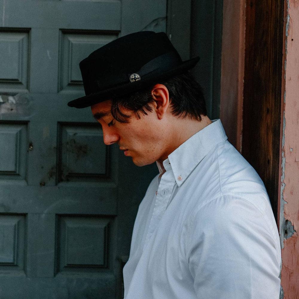 A man leaning on a wall wearing Chi-Town Black Felt Pork Pie 