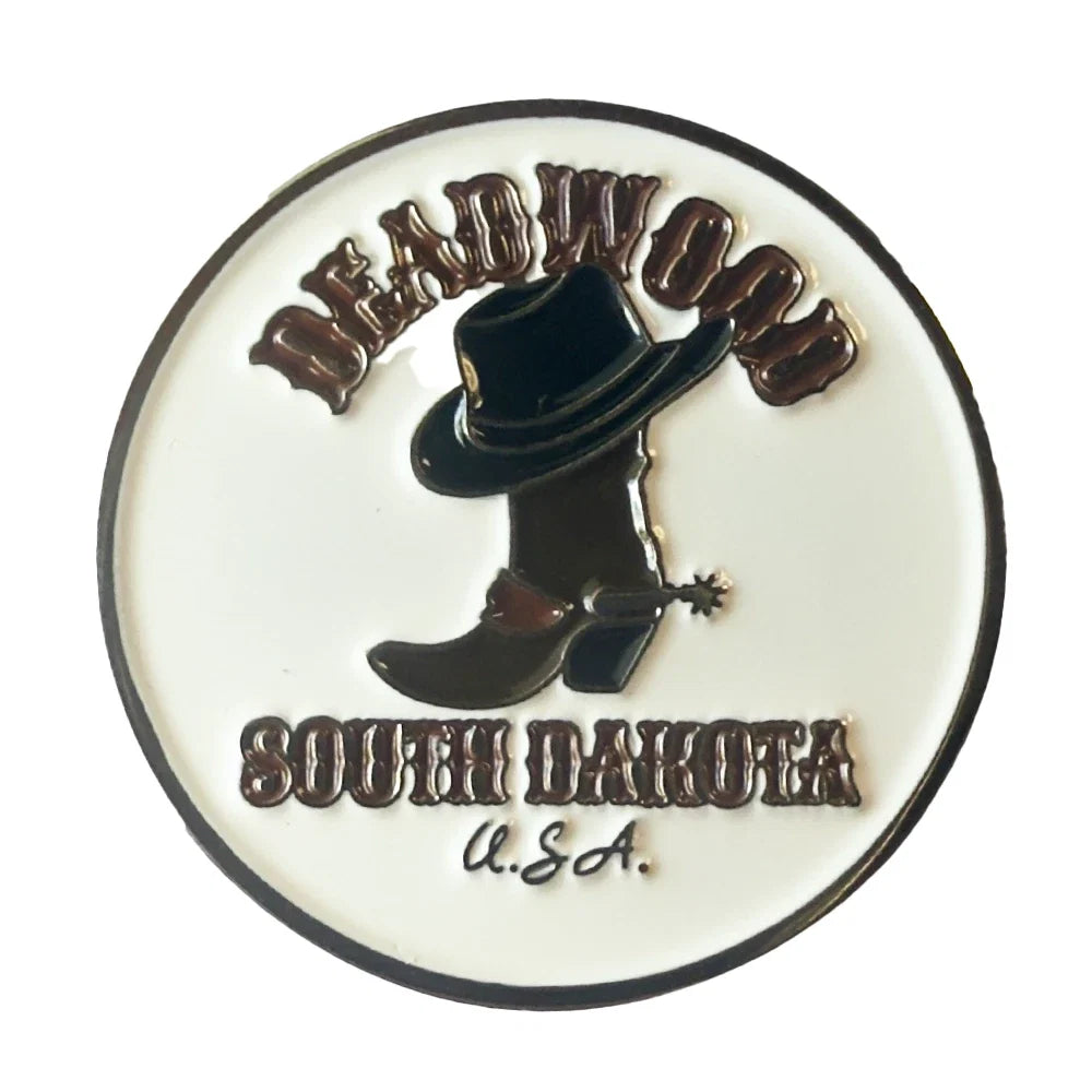 A circular enamel pin featuring a black cowboy hat and boot with a spurs detail on a white background, with the text 'DEADWOOD SOUTH DAKOTA U.S.