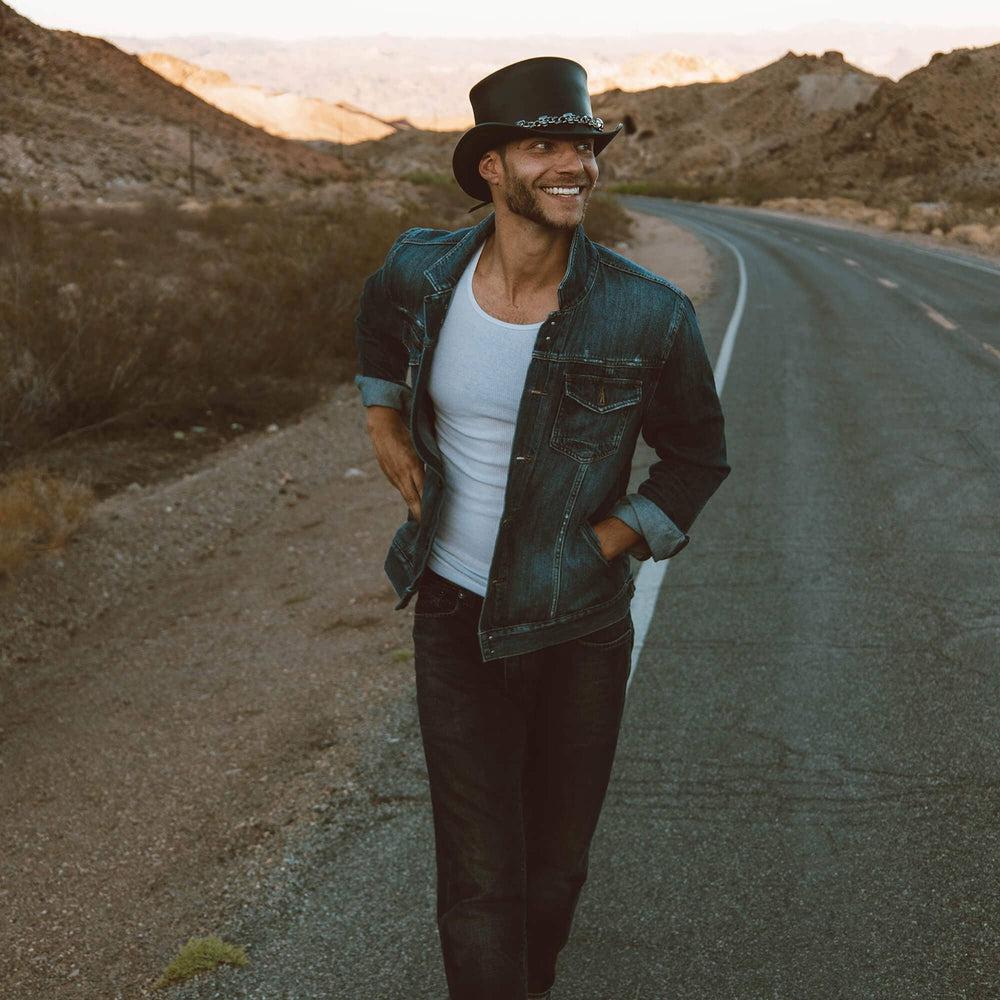  A man walking in the streets wearing El Dorado Black Leather Top Hat with a 5 Skull Band