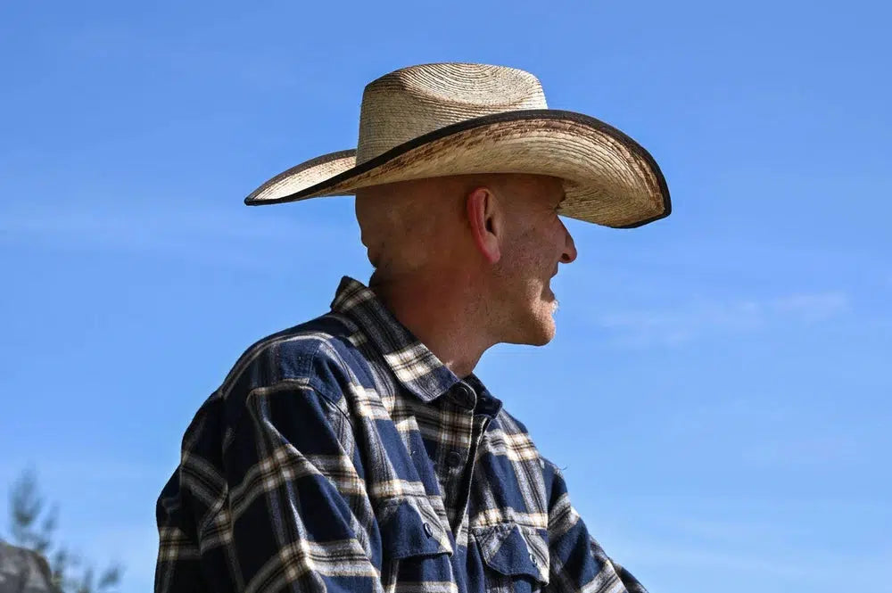 A man wearing a blue plaid polo and a brown straw cowboy hat