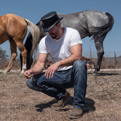 A man in white shirt and black top hat with horses on the background 