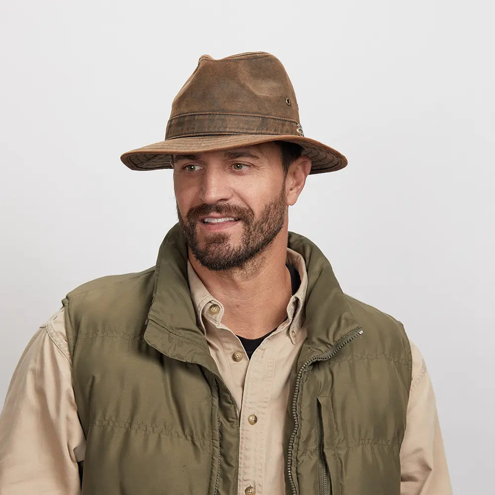 Smiling man wearing a brown Otis leather hat and a green outdoor jacket over a beige shirt.