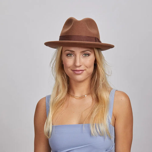 Portrait of a smiling woman with blonde hair, wearing a brown Pablo fedora and a blue sleeveless top.