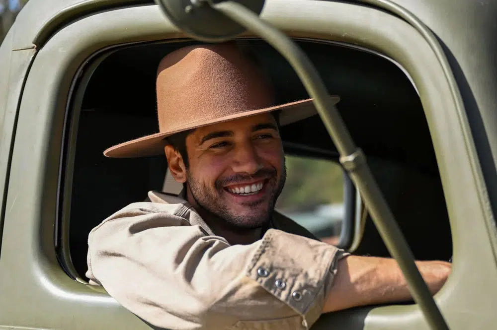 A man sitting inside a truck wearing a polo and a brown felt hat