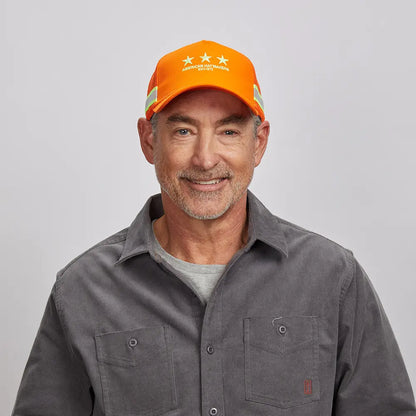 A smiling old man wearing an orange mesh cap and gray polo