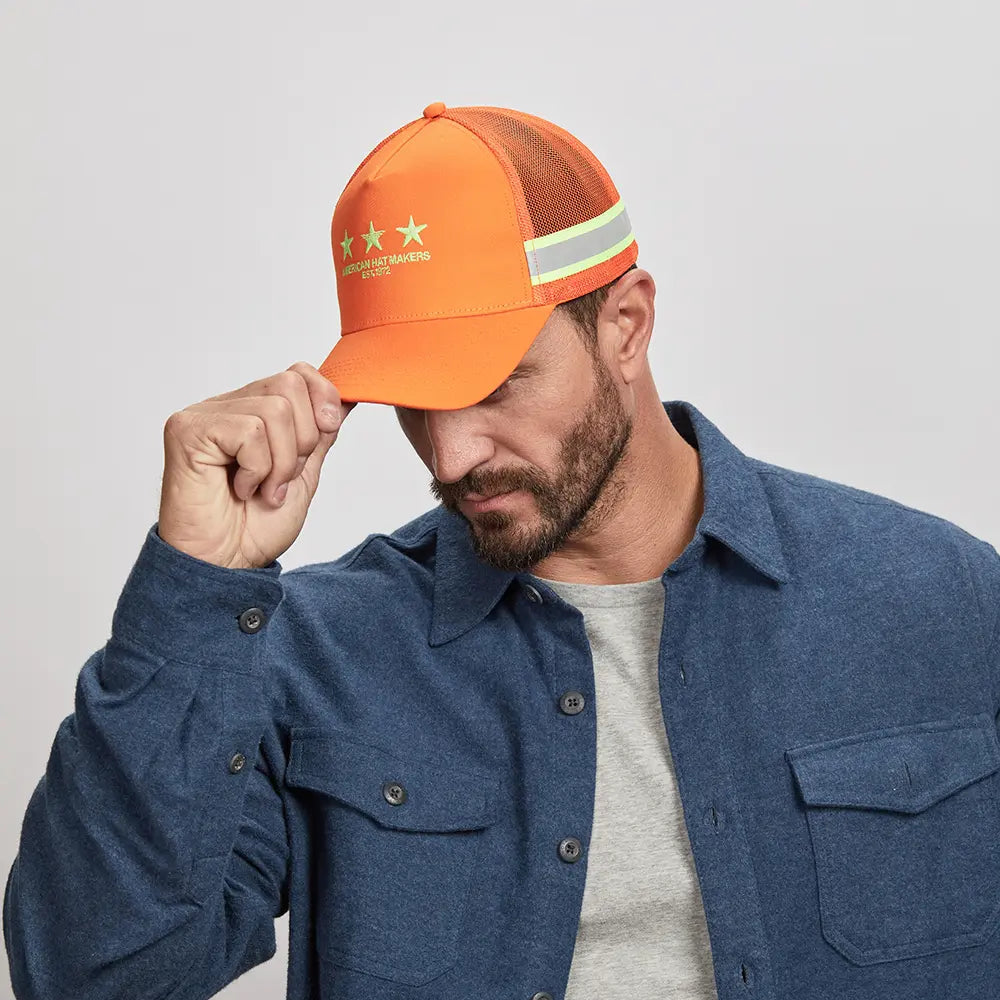 A man holding his orange cap wearing an blue polo over a white shirt