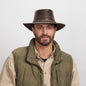 Man with a light stubble wearing a Chocolate Roughneck Outback Hat and an olive green jacket over a beige shirt