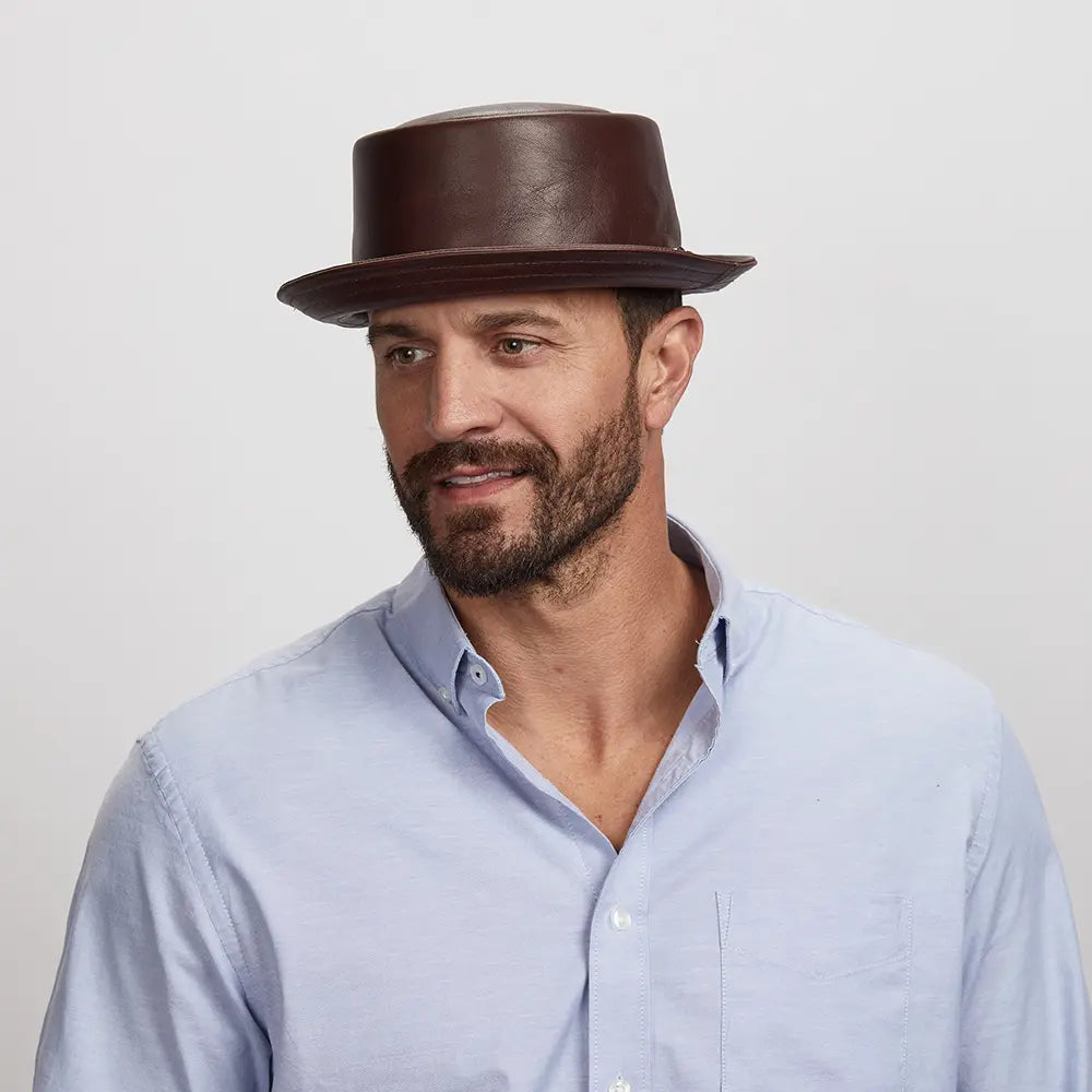 A young man looking to the side wearing a brown leather hat