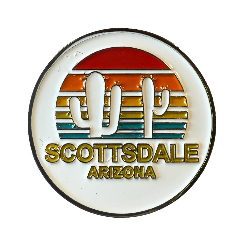 A circular enamel pin featuring a retro sunset design with a white cactus silhouette, horizontal stripes in red, orange, yellow, and teal, and the text 'SCOTTSDALE ARIZONA' in gold lettering.