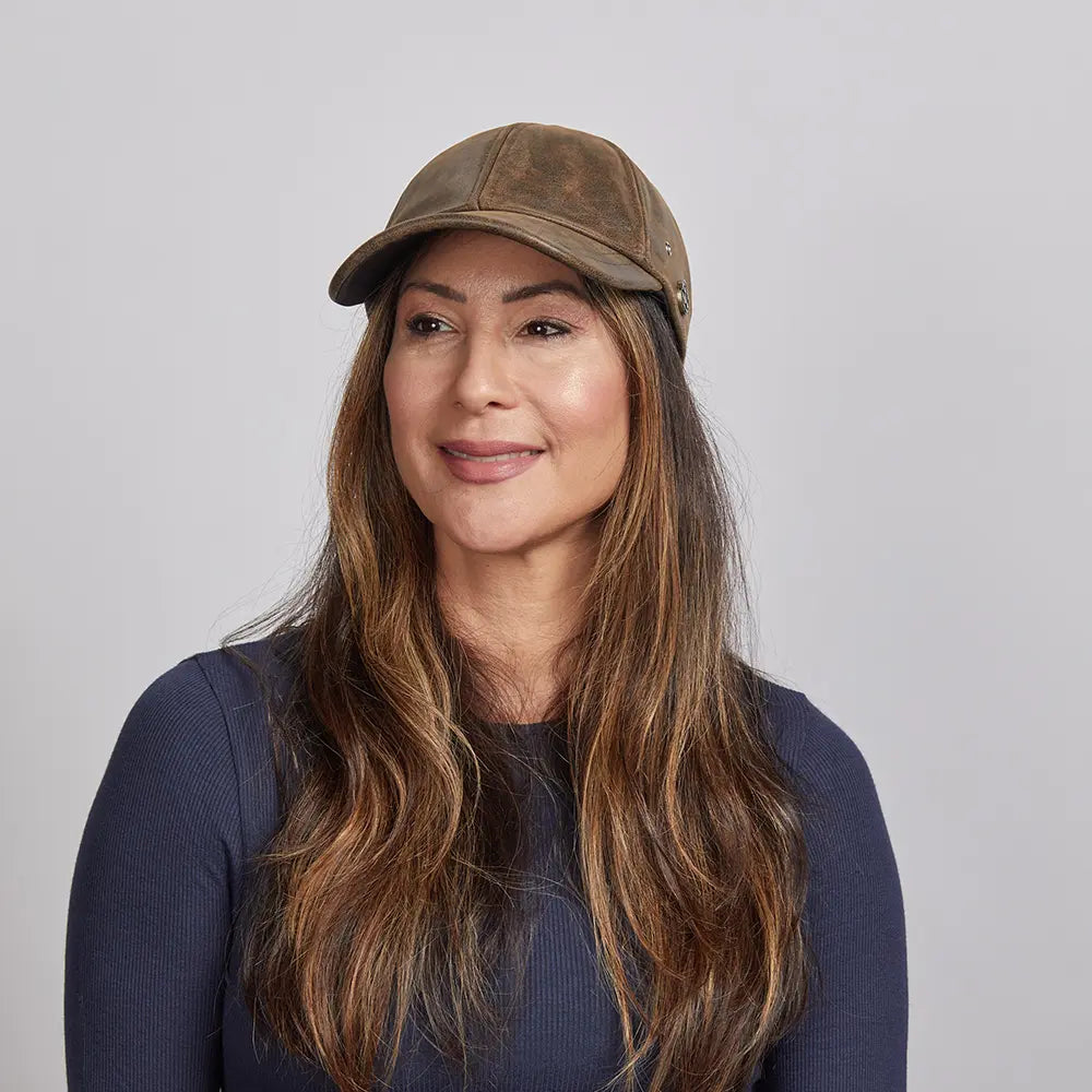 A woman slightly smiling wearing a brown leather cap and a navy blue top