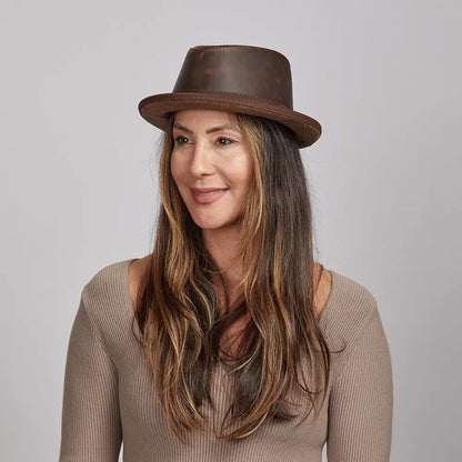 Woman with long brown hair wearing a brown leather hat and a beige top looking afar