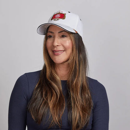 A woman with long brown hair smiling, wearing a white Stay Humble cap and a navy blue top.