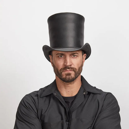 A man with stubble wearing a unique black stove piper hat and a black shirt.