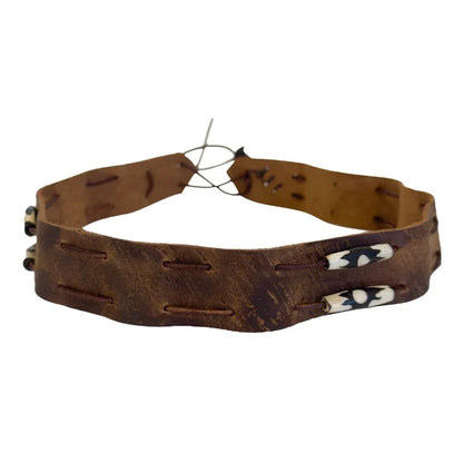 A distressed brown leather belt with decorative stitched holes and two cowrie shells on the front, displayed on a solid white background.